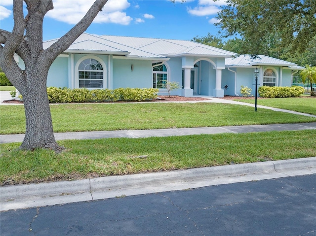 single story home with metal roof, a front lawn, and stucco siding