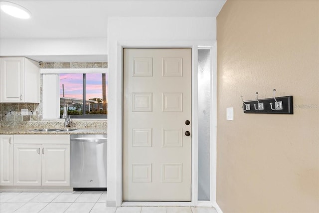 kitchen with light tile patterned floors, white cabinets, dishwasher, light stone counters, and a sink