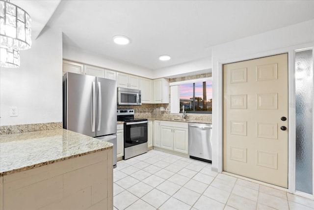 kitchen with light tile patterned floors, light stone countertops, stainless steel appliances, hanging light fixtures, and decorative backsplash