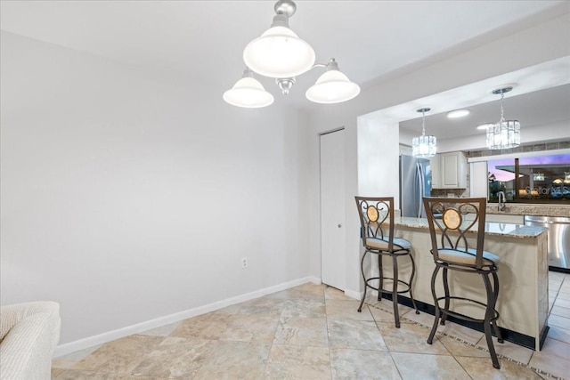 kitchen featuring a peninsula, light stone countertops, stainless steel appliances, a kitchen bar, and pendant lighting