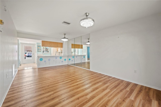 unfurnished living room with light wood-style floors, visible vents, and a sink