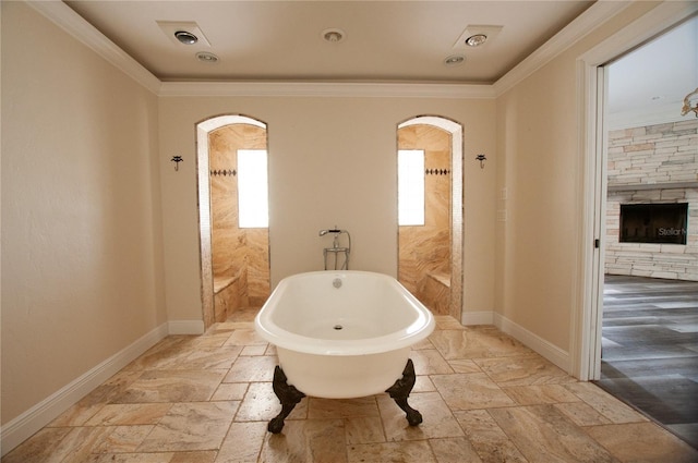 bathroom with crown molding, stone tile flooring, a soaking tub, and baseboards