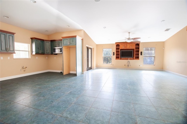 unfurnished living room featuring ceiling fan, dark tile patterned floors, a wealth of natural light, and baseboards