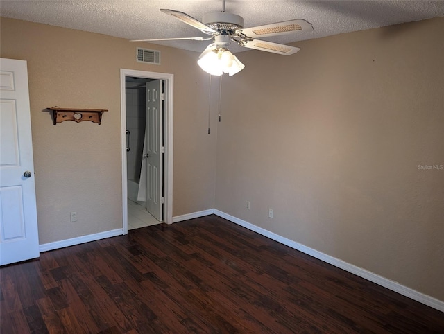 empty room with a textured ceiling, wood finished floors, visible vents, and baseboards