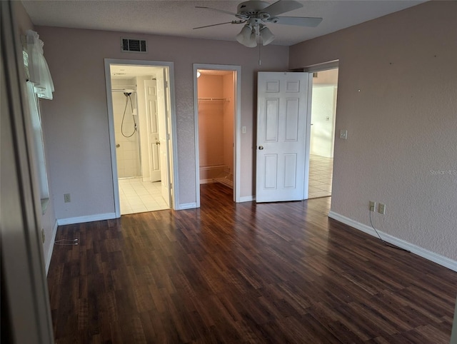 unfurnished bedroom with dark wood-style floors, a walk in closet, a closet, visible vents, and baseboards