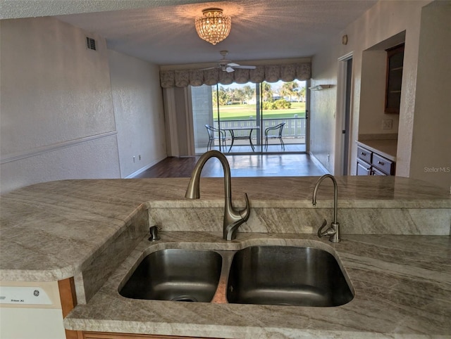 kitchen featuring light countertops, a textured wall, visible vents, a sink, and a textured ceiling