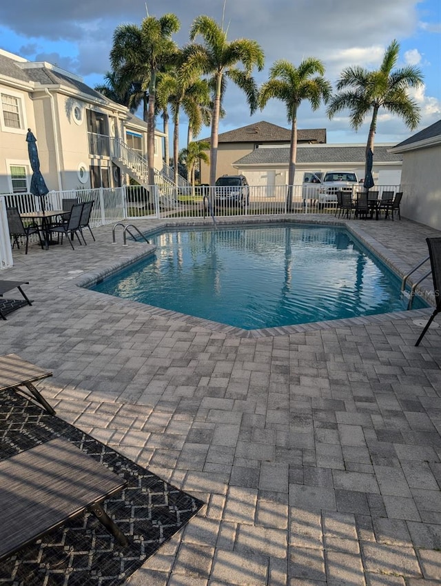 community pool with a patio area, fence, and outdoor dining space