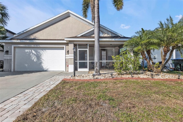 view of front of home with concrete driveway, a sunroom, an attached garage, a front lawn, and stucco siding