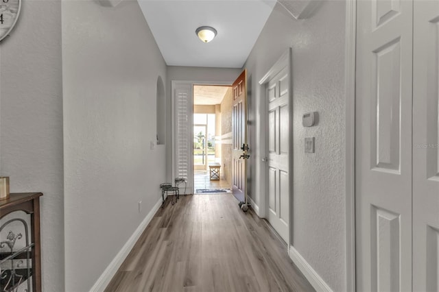 corridor featuring baseboards, arched walkways, wood finished floors, and a textured wall