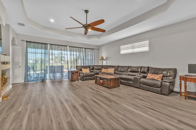 living room featuring a tray ceiling, a healthy amount of sunlight, and light wood finished floors