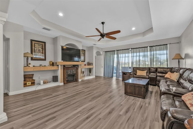 living room featuring visible vents, a ceiling fan, a tiled fireplace, light wood-style flooring, and a tray ceiling