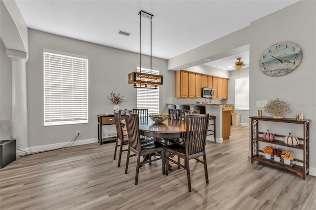 dining room with light wood finished floors, baseboards, and ornate columns