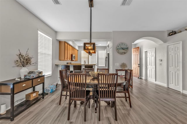 dining space with arched walkways, light wood-style flooring, visible vents, and baseboards