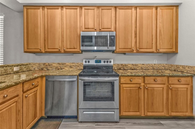 kitchen featuring appliances with stainless steel finishes, light wood-style flooring, and light stone countertops