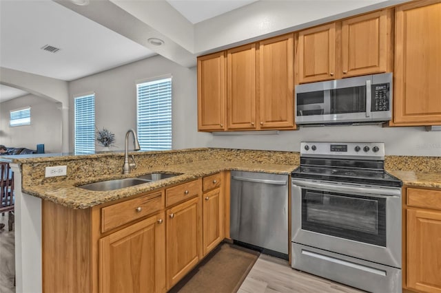 kitchen with light stone counters, a peninsula, a sink, visible vents, and appliances with stainless steel finishes