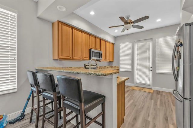 kitchen featuring a breakfast bar, light wood-style flooring, baseboards, and stainless steel appliances