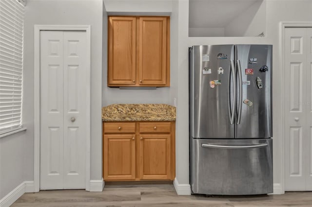 kitchen with light stone counters, light wood-type flooring, freestanding refrigerator, and baseboards