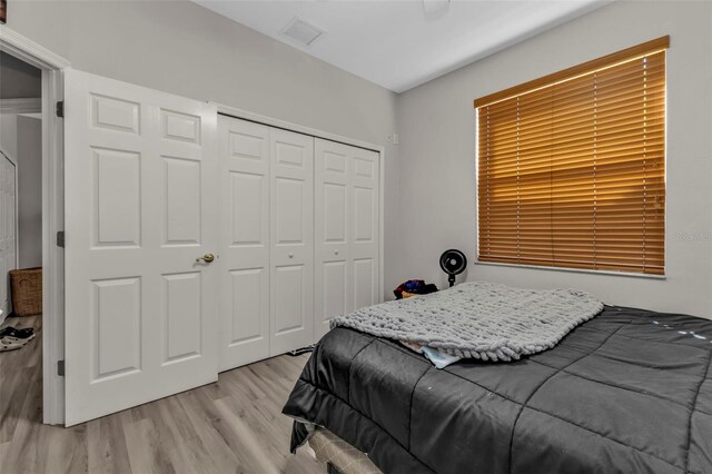 bedroom with light wood-type flooring, visible vents, and a closet