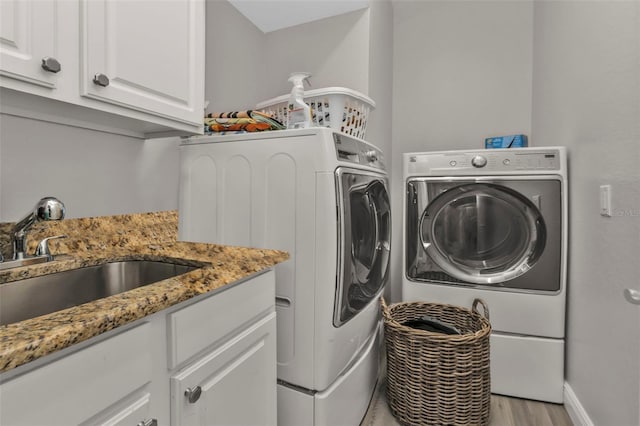 clothes washing area featuring cabinet space, light wood-style flooring, a sink, independent washer and dryer, and baseboards