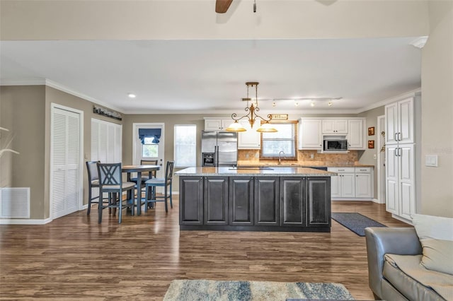 kitchen with visible vents, a kitchen island, appliances with stainless steel finishes, decorative light fixtures, and crown molding