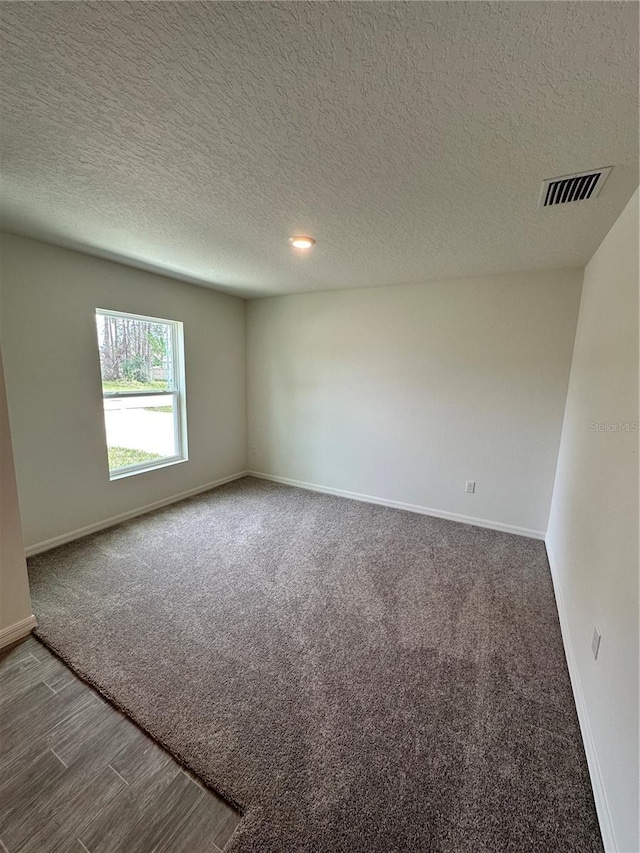 spare room with a textured ceiling, wood finished floors, visible vents, and baseboards