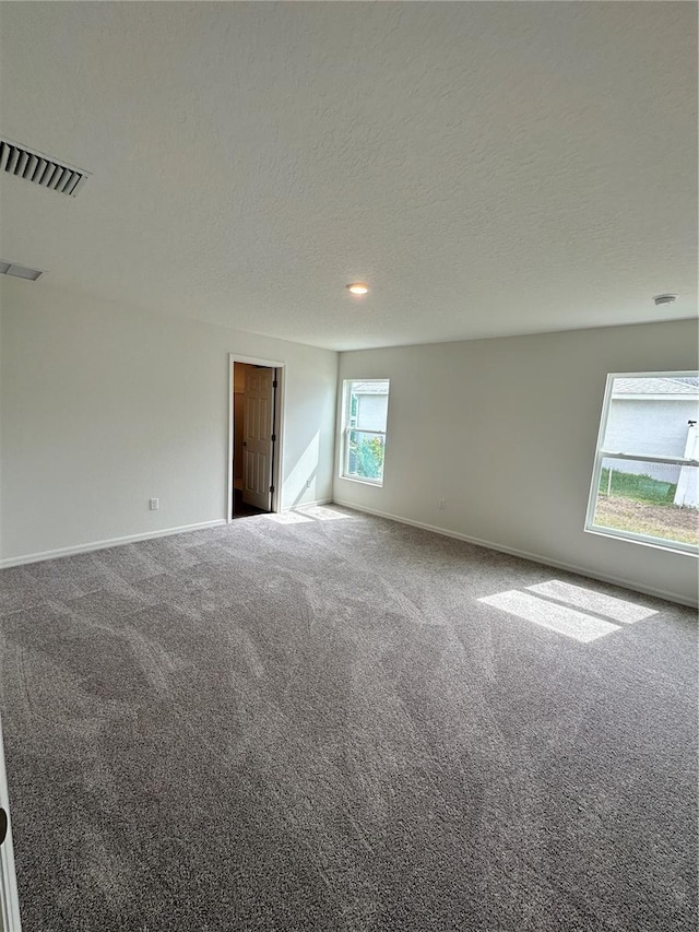 spare room with a textured ceiling, carpet flooring, visible vents, and baseboards