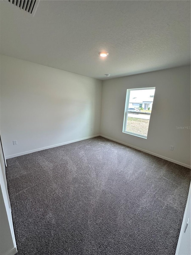 unfurnished room with a textured ceiling, dark carpet, visible vents, and baseboards