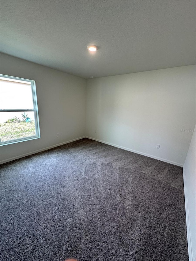 empty room with dark colored carpet, a textured ceiling, and baseboards