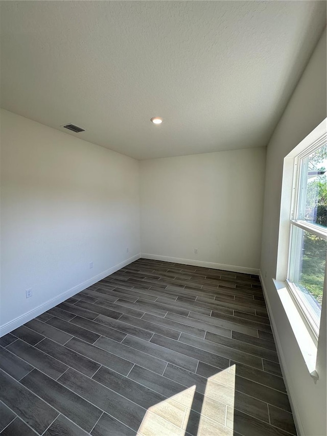 empty room featuring a textured ceiling, wood tiled floor, visible vents, and baseboards