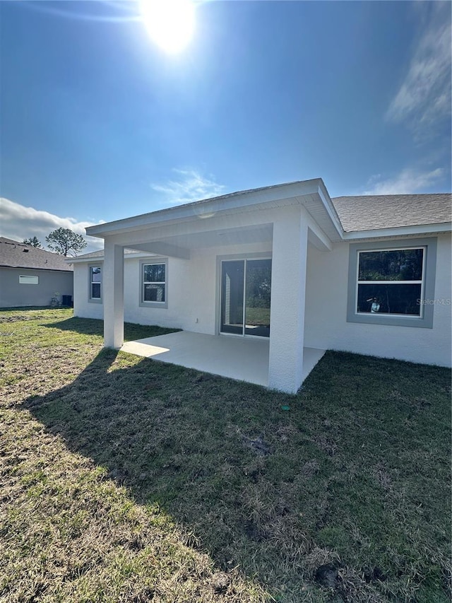 rear view of house with roof with shingles, a lawn, a patio area, and stucco siding