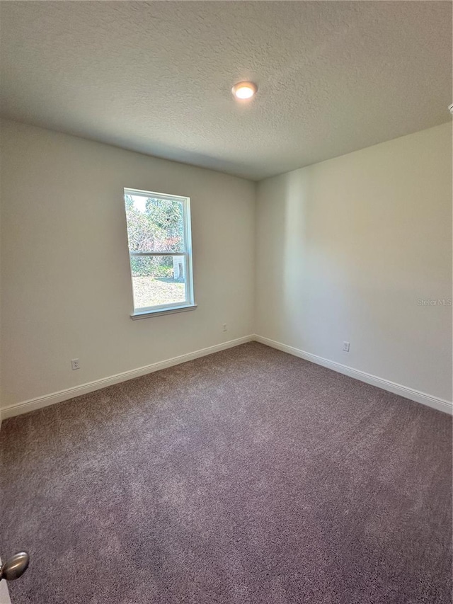 carpeted spare room featuring a textured ceiling and baseboards