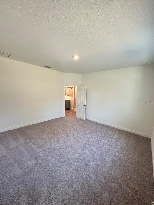 carpeted empty room with baseboards, visible vents, and a textured ceiling