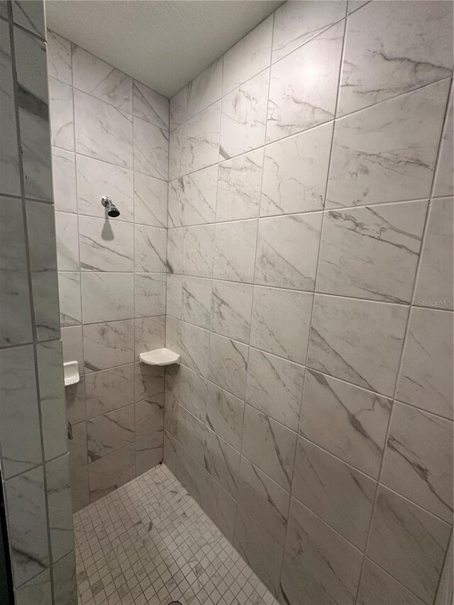 bathroom with a textured ceiling and tiled shower