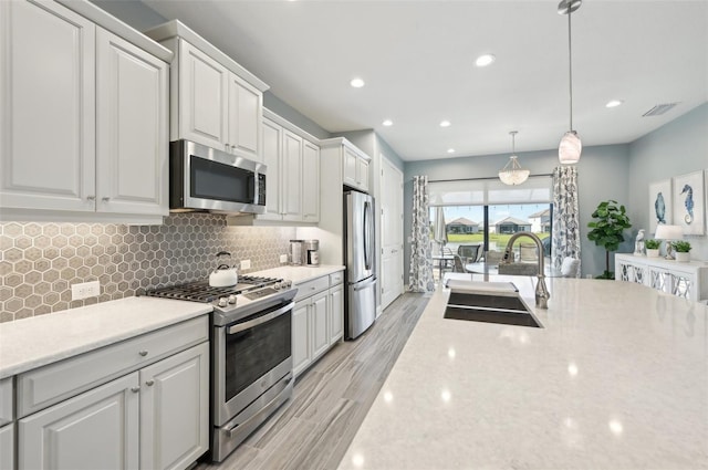 kitchen with a sink, visible vents, white cabinets, appliances with stainless steel finishes, and decorative backsplash