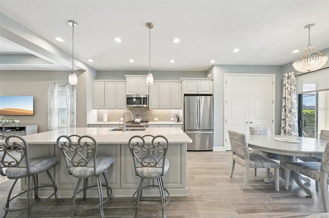 kitchen featuring tasteful backsplash, a kitchen island with sink, stainless steel appliances, light countertops, and a sink