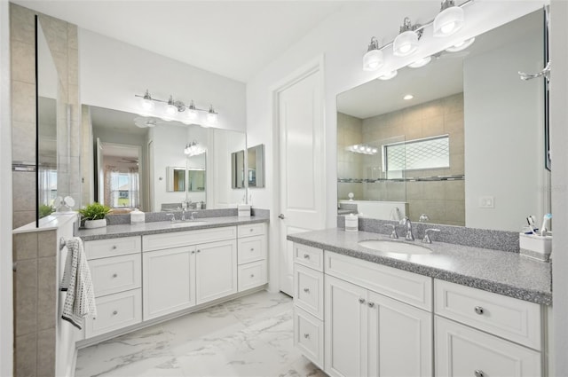 bathroom featuring marble finish floor, two vanities, a tile shower, and a sink