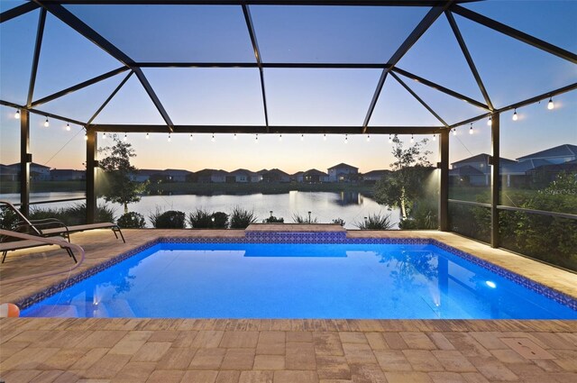 pool at dusk featuring glass enclosure, a patio area, an outdoor pool, and a water view