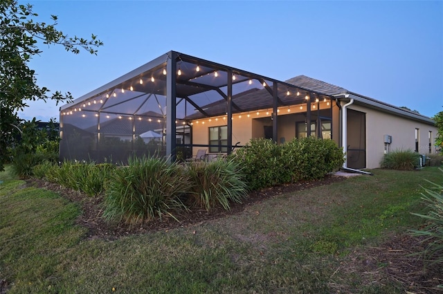 rear view of house featuring a lanai, a yard, and stucco siding