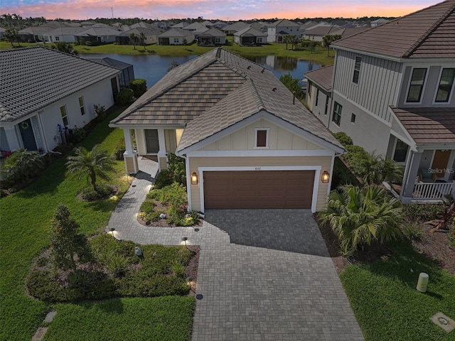 view of front of house with decorative driveway, a water view, an attached garage, board and batten siding, and a residential view