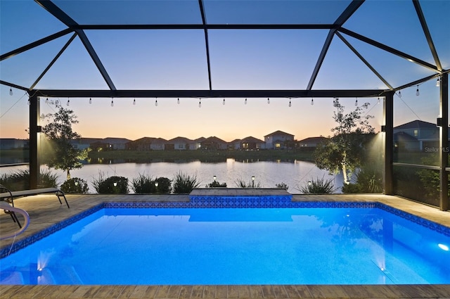 pool at dusk featuring a water view, a patio area, a lanai, and an outdoor pool