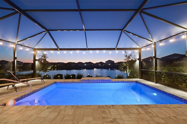 outdoor pool with glass enclosure, a patio area, and a water view