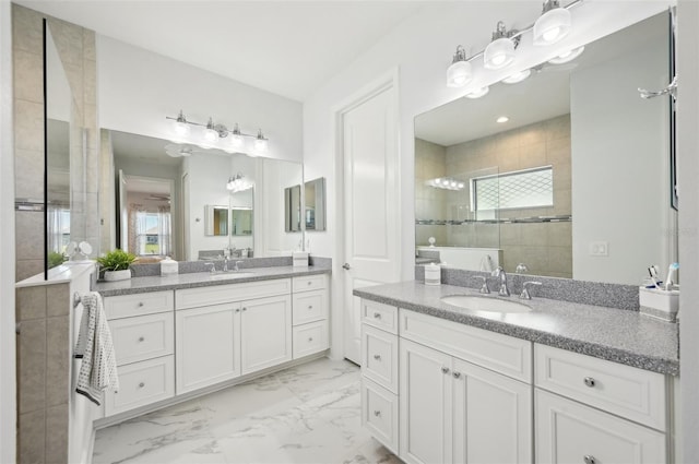 full bathroom with marble look tile flooring, tiled shower, plenty of natural light, and two vanities