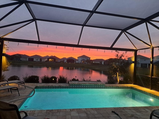 pool at dusk featuring a water view, a patio, an outdoor pool, and a lanai