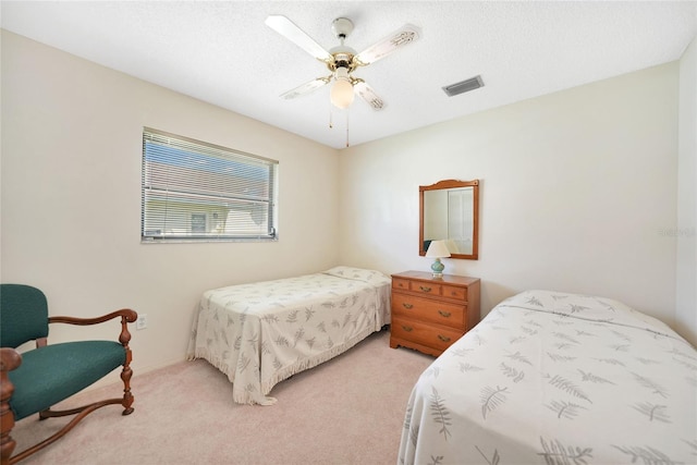 bedroom with a textured ceiling, a ceiling fan, visible vents, and light colored carpet