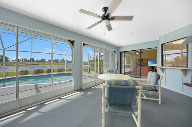 sunroom featuring ceiling fan and a water view