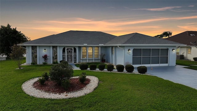 ranch-style home with a yard, stucco siding, an attached garage, central AC unit, and driveway