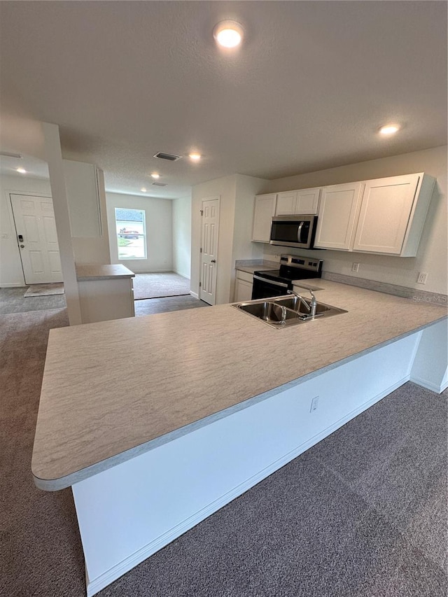 kitchen with stainless steel microwave, dark carpet, electric range, white cabinets, and a peninsula