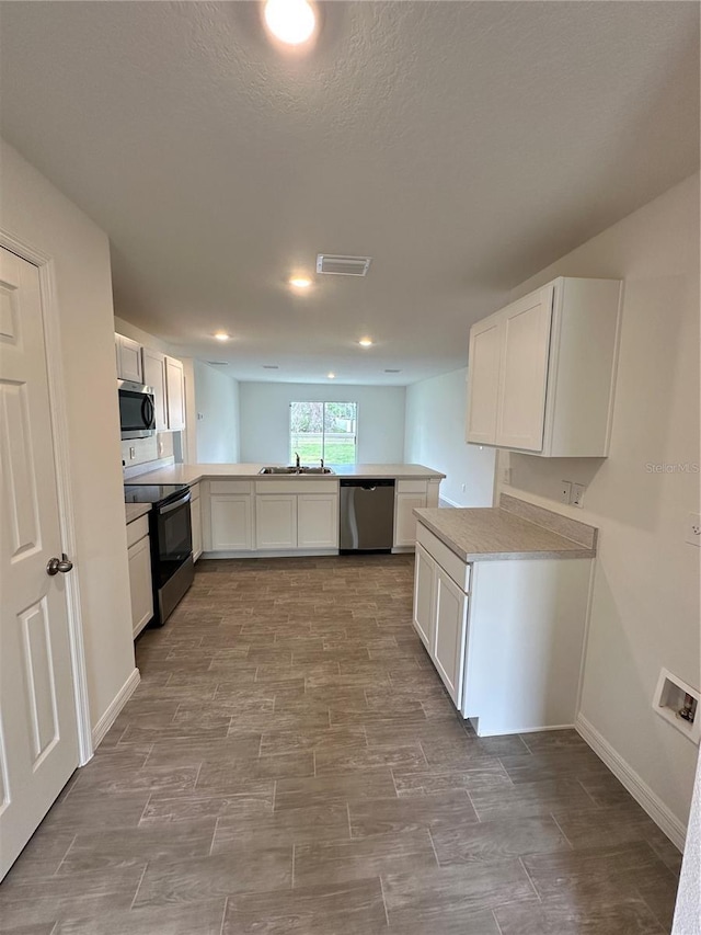 kitchen with a peninsula, white cabinets, stainless steel appliances, and light countertops