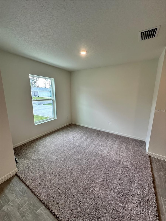 unfurnished room with a textured ceiling, carpet floors, visible vents, and baseboards