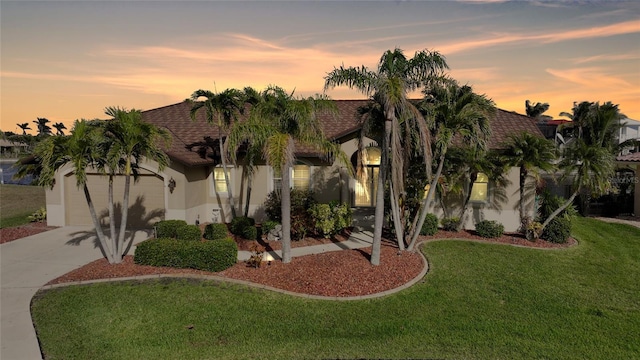 view of front facade featuring an attached garage, a shingled roof, driveway, a yard, and stucco siding